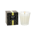 A lit Nest New York Grapefruit candle in a white striped glass jar sits next to its decorative black and gold bestselling fragrance box.