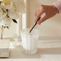 A hand uses a long match to light the wick of a striped glass Nest New York Grapefruit Candle set next to a bouquet of white flowers.