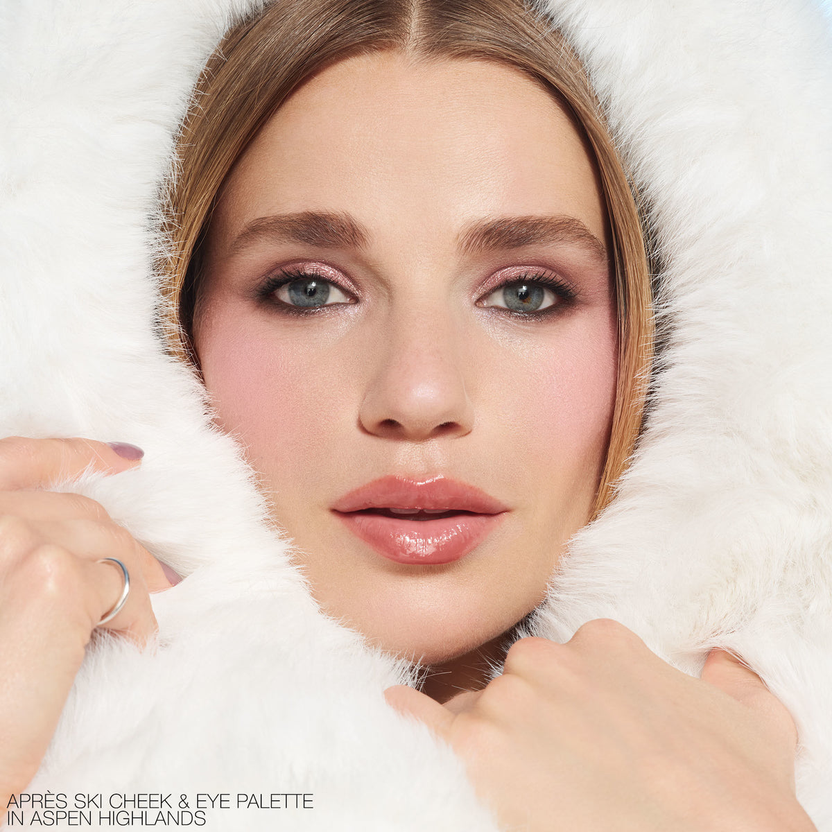 Close-up of a woman in an après style white fur-trimmed hood, wearing vibrant pink eyeshadow and blush from the Nars Après Ski Cheek & Eye Palette.