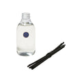 A clear glass Joséphine Diffuser bottle filled with floral fragrance oil alongside a bundle of black reed diffuser sticks.
