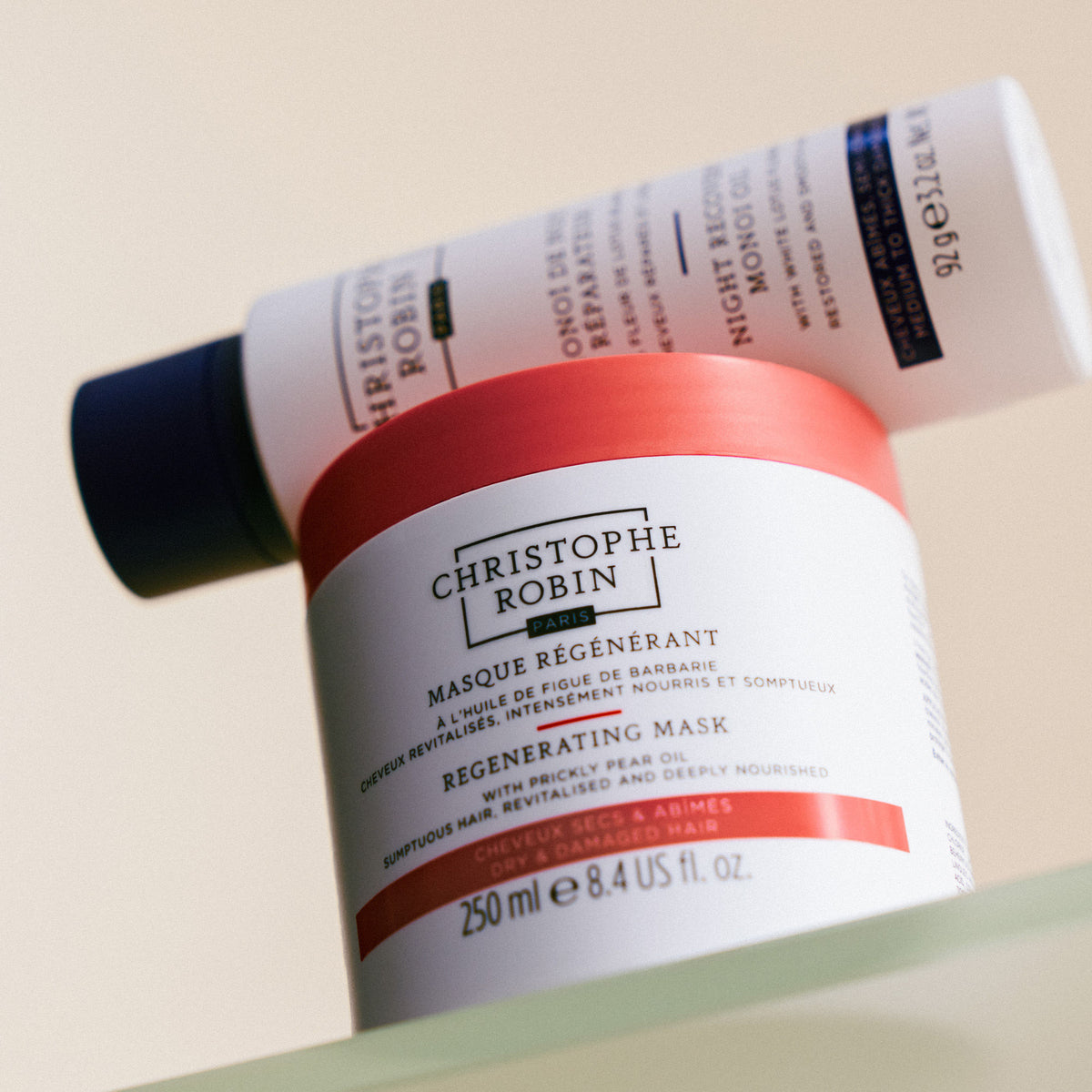 A jar of Night Recovery Monoï Oil with White Lotus Flower regenerating mask with a tube of intensive treatment oil balanced on top to strengthen and protect hair.