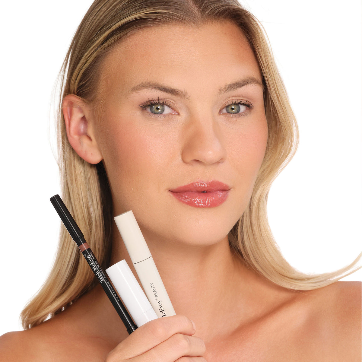 A woman with naturally fuller, glossy nude lips holds the Trish McEvoy The Bluemercury Exclusive Plump, Protect & Perfect Nude Lip Wardrobe (Limited Edition) lip liner and two tubes of lip products to achieve lip perfection.