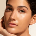 Close-up of a person with glowing, dewy skin enhanced by Jane Iredale Glow Fixation SPF 40 Sheer Tint Skin Enhancer with Squalane & Niacinamide, resting their chin on their hand.