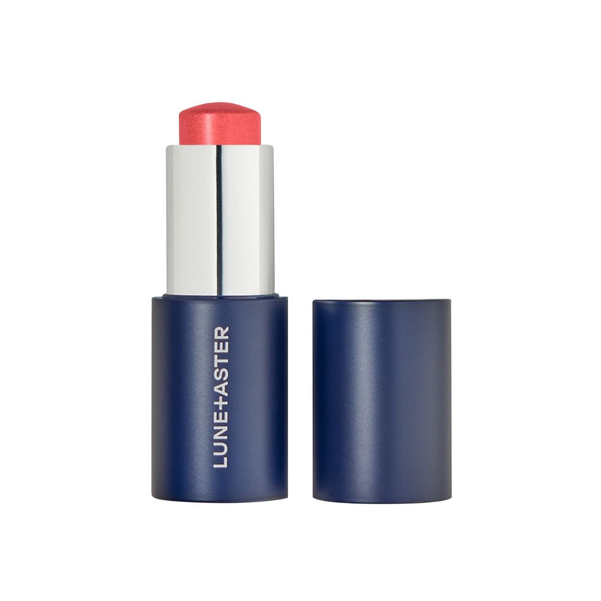 A coral-colored Lune+Aster Cream Multi-Stick in a navy blue tube with its matching cap resting beside it.