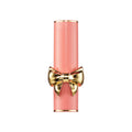 A cylindrical light pink SatinAllure Lipstick tube featuring a prominent gold bow, designed to veil your lips in weightless, silky smooth color.