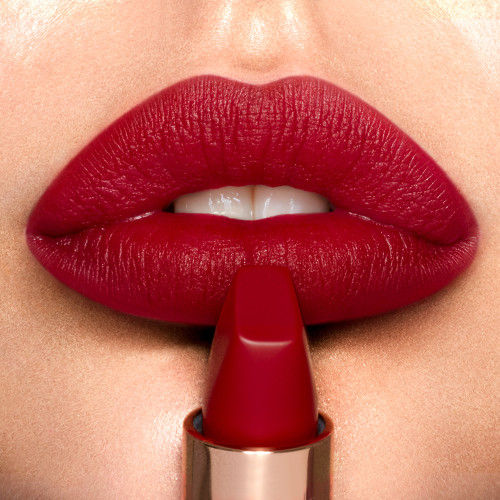 Close-up of lips painted in a long-lasting, matte red Charlotte Tilbury Matte Revolution lipstick, with an open tube of the same matching shade held in front.