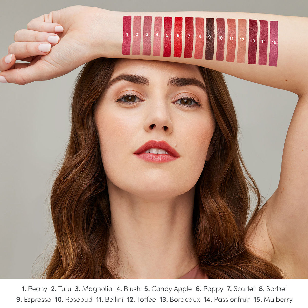 A woman displays fifteen numbered satin finish ColorLuxe Hydrating Cream Lipstick swatches on her arm, with a key listing the corresponding color names below.